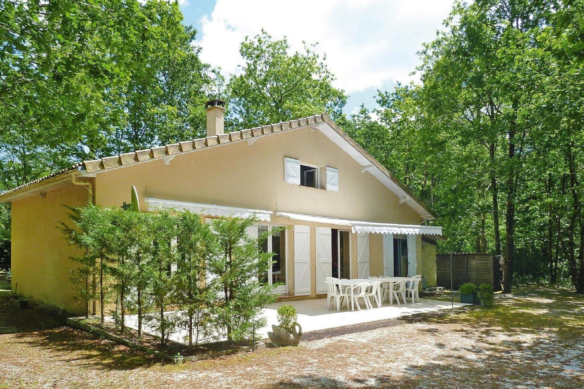 Uma casa térrea com fachada bege, chaminé e um espaço de varanda coberto com mobiliário branco.
