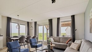 Un salon moderne avec un coin repas, de grandes fenêtres et une vue sur l’extérieur.