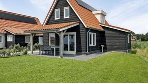 Une maison moderne avec une façade sombre, un toit en pente et un patio couvert.