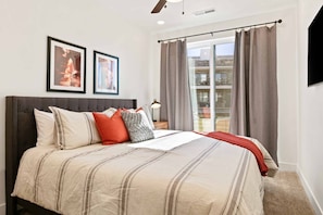 A bedroom with a large bed, a nightstand, two framed pictures, and a view of a balcony.
