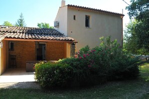 Una casa de dos pisos con techo de tejas, un balcón pequeño y un jardín con plantas florecientes.