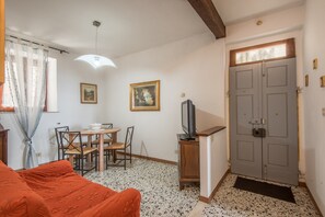 A room with a bed, a dining table with chairs, a television on a stand, and a door with a window above it.