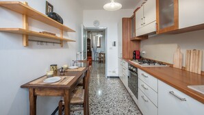 Une cuisine avec des étagères en bois, une table à manger avec des chaises, une cuisinière et un réfrigérateur.