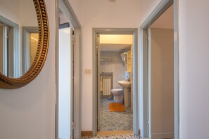 Ein Flur, der zu einem Badezimmer mit Toilette, Waschbecken und Spiegel führt.