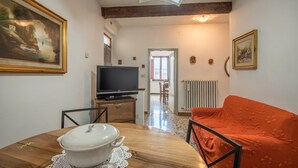 Un coin repas avec une table en bois, un pot blanc et un téléviseur posé sur un meuble en bois.
