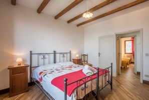 A bedroom with a bed, bedside tables, a wooden cabinet, a hanging light fixture, and a door leading to another room.