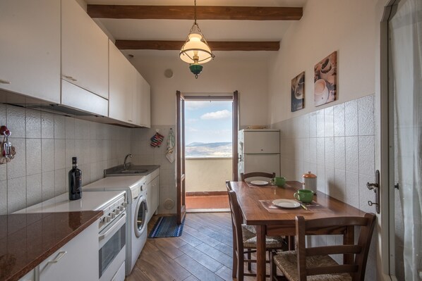 A compact kitchen with a dining area, a washing machine, and a view through an open door.