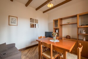A dining area with a wooden table, chairs, a vase with flowers, a framed picture, and a television on a stand.