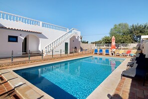 A swimming pool with a tiled deck, a staircase, and lounge chairs.