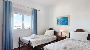 Une chambre d’hôtel avec deux lits, une table de chevet, une lampe, un tableau et une fenêtre avec des rideaux.