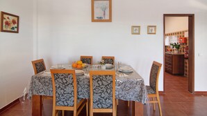 Un coin repas avec une table dressée pour quatre personnes, des chaises et une cuisine visible à travers une porte ouverte.