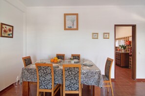 A dining area with a table set for four, chairs, and a kitchen visible through an open doorway.