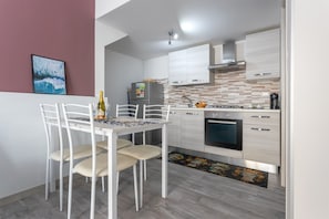 Une cuisine moderne avec des armoires blanches, un four encastré et un coin repas comprenant une table et des chaises.