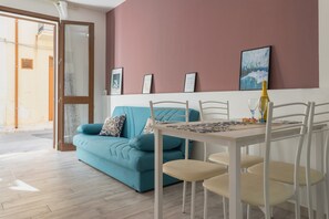 Une pièce avec un canapé de couleur turquoise, une table à manger blanche avec des chaises, une bouteille en verre et des tableaux encadrés accrochés au mur.