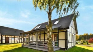 A traditional half-timbered house with a sloped roof, a wooden deck, and a well-maintained lawn. - Holiday studio with terrace (Jaroslawiec)