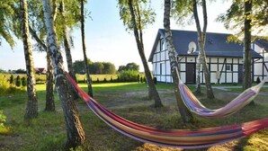 A hammock in a grassy area with trees and a building in the background. - Holiday studio with terrace (Jaroslawiec)