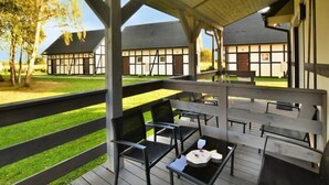 A covered outdoor seating area with wooden benches and tables, overlooking a traditional building with exposed timber framing. - Holiday studio with terrace (Jaroslawiec)