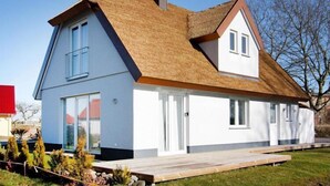 Ein modernes Haus mit einem Strohdach, großen Fenstern und einer Holzterrasse.