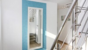 Ein modernes Interieur mit blauer Akzentwand, einem großen Spiegel, der eine Treppe reflektiert, und einem Metallgeländer.