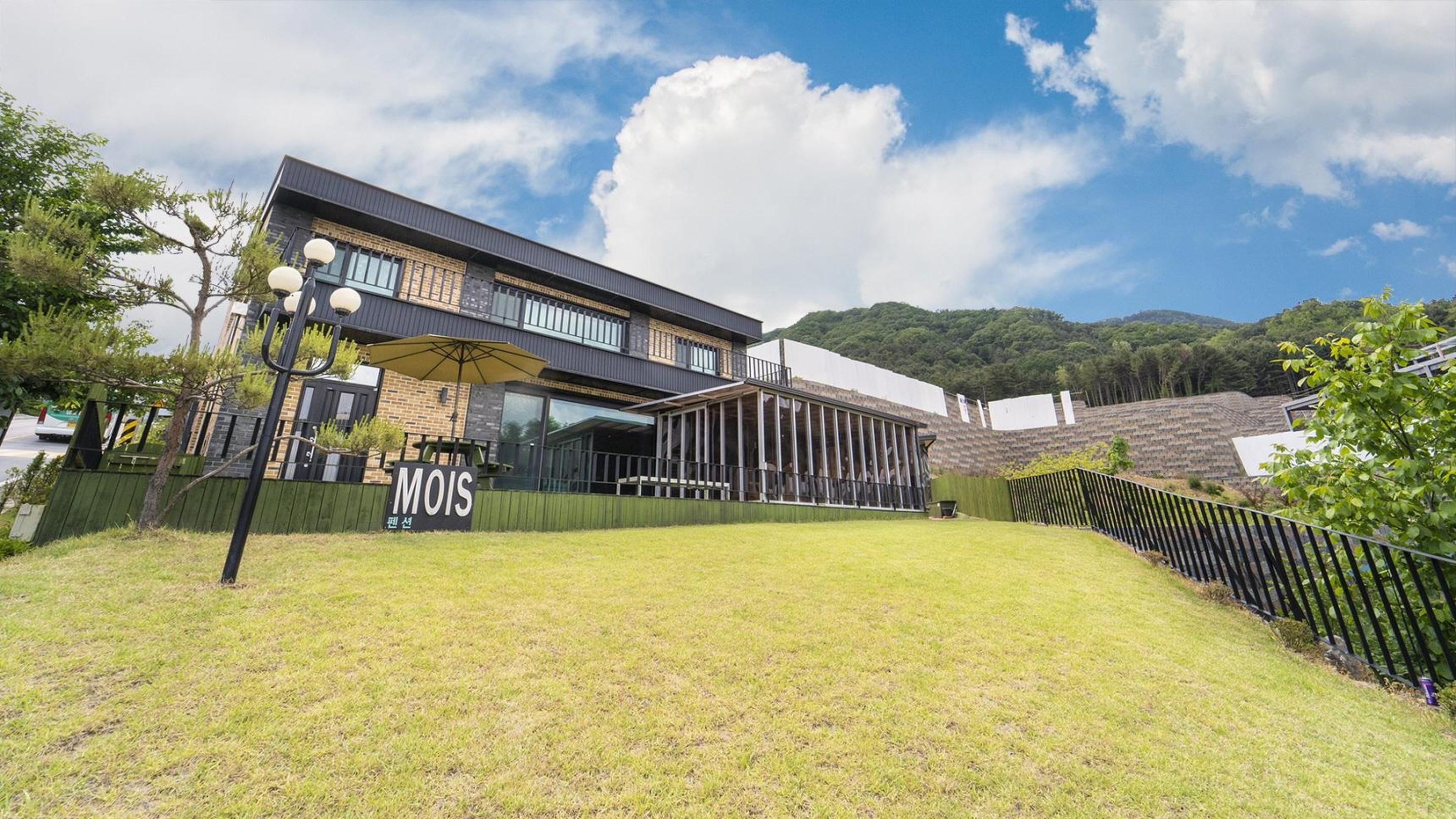 A modern building with a glass facade, a sign reading "MOIS," and a grassy area in front.