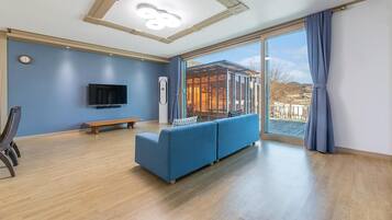 A modern living room with a blue sofa, a wooden bench, a flat-screen TV, and a large sliding glass door leading to an outdoor area.