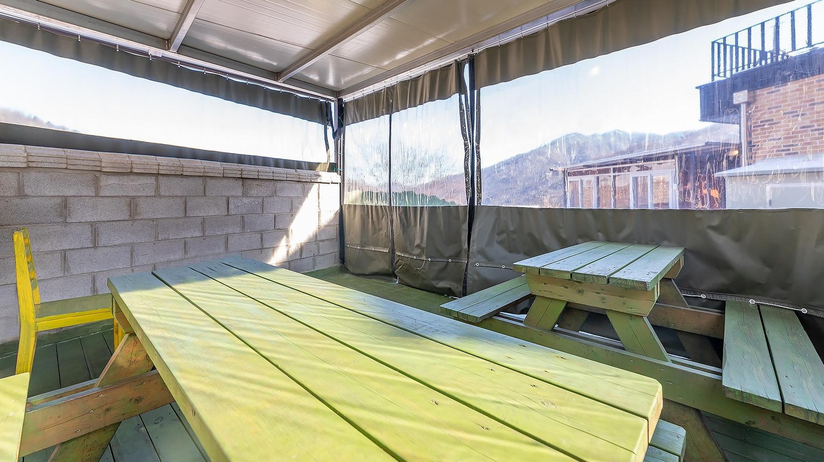 Eine Terrasse im Freien mit Holztisch und -bänken, einer Backsteinmauer und Blick auf Berge.