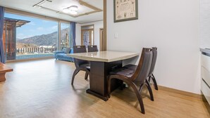 Un coin repas avec une table et des chaises, de grandes fenêtres offrant une vue sur les montagnes, et un canapé bleu en arrière-plan.