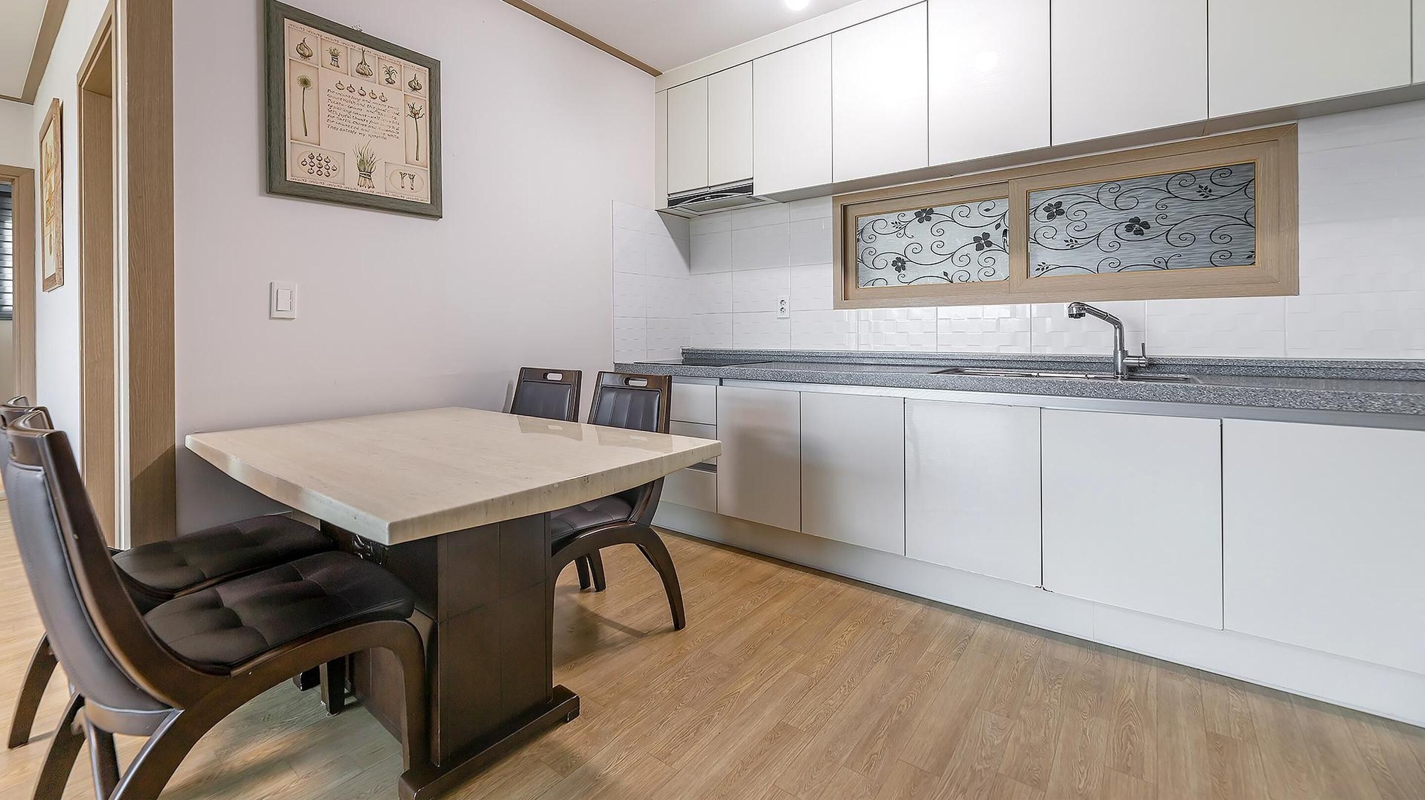 Una cucina moderna con mobili bianchi, un piano di lavoro in granito e un'area pranzo con tavolo e sedie.