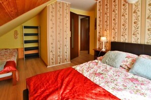 Een slaapkamer met een schuine plafond, een bed met bloemenbeddengoed, een rode plaid en een nachtkastje met een lamp.