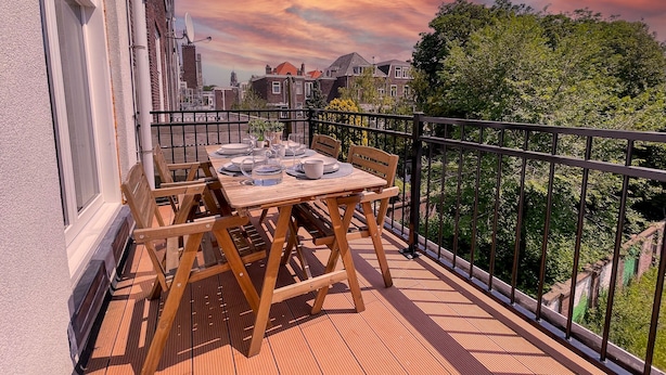 A wooden deck with a table set for dining, surrounded by a black metal railing. - LVM Stays (The Hague)