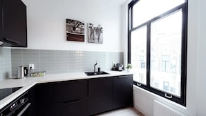 A modern kitchen with black cabinets, a white countertop, a black sink, and a window with a view of buildings. - LVM Stays (The Hague)