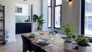 A dining area with a wooden table set for four, surrounded by large windows and potted plants. - LVM Stays (The Hague)