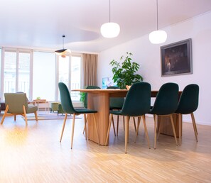Ein moderner Besprechungsraum mit Holztisch, grünen Stühlen und einem Blumentopf.