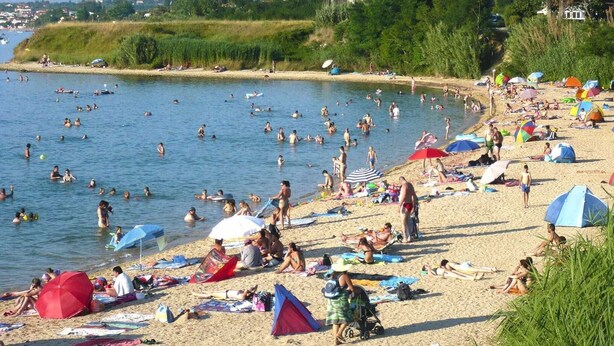 Een druk strand met mensen die zwemmen en zonnebaden, tenten en parasols.