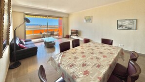A spacious room with a large table, a sofa, a TV, and a balcony with a view. - Ajaccio: Air-conditioned 4-room apartment, 6 beds, downtown (Ajaccio)