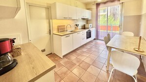 A compact kitchen with white cabinets, a sink, a microwave, and a dining area with a table and chairs. - Ajaccio: Air-conditioned 4-room apartment, 6 beds, downtown (Ajaccio)