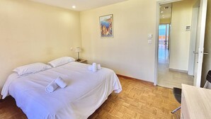 A hotel room with a bed, a nightstand, a lamp, a poster on the wall, and a door leading to another room. - Ajaccio: Air-conditioned 4-room apartment, 6 beds, downtown (Ajaccio)