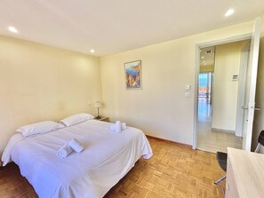 Une chambre d’hôtel avec un lit, une table de chevet, une lampe, une affiche au mur et une porte donnant sur une autre pièce.