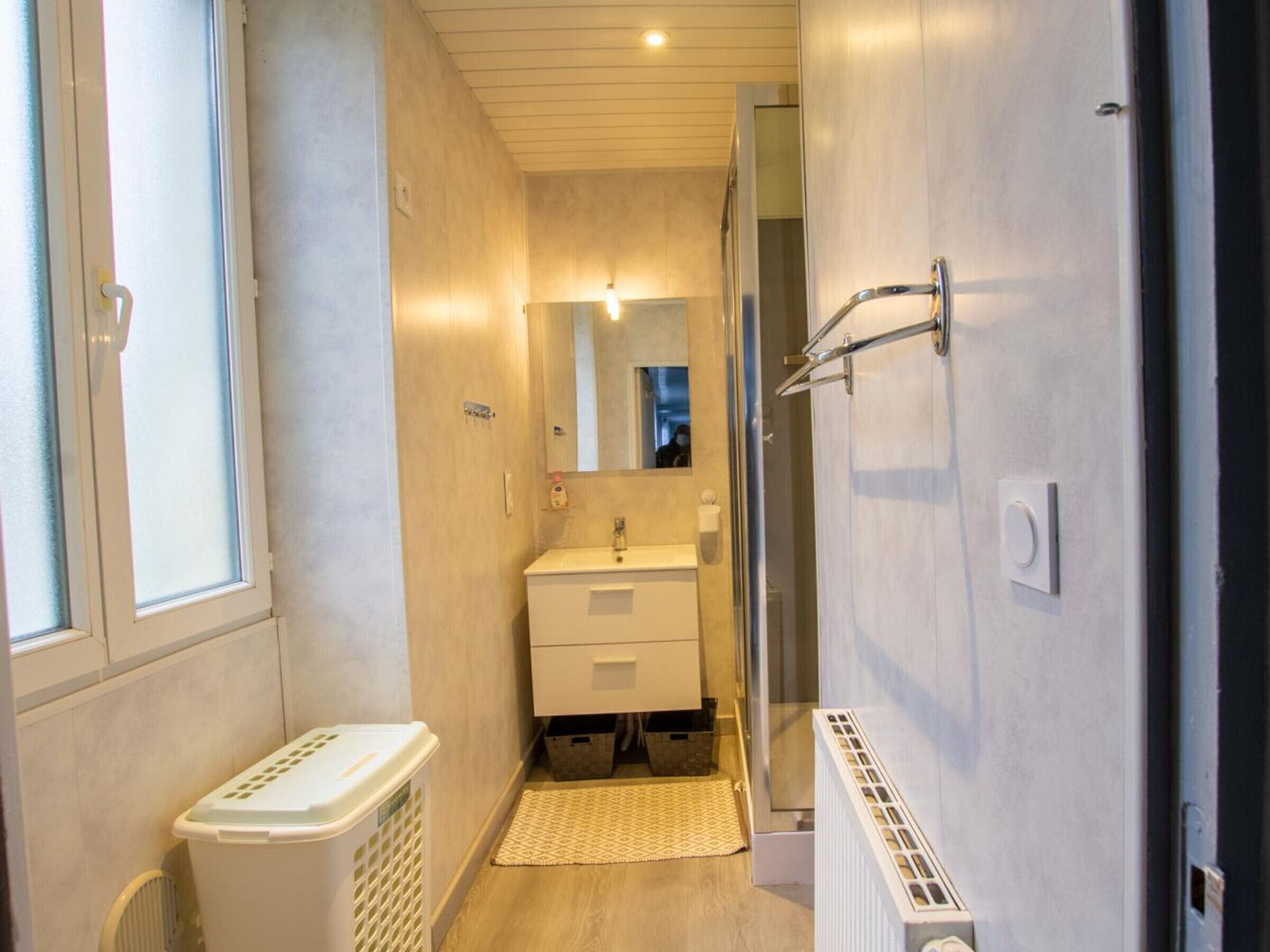 A narrow, well-lit bathroom with a single sink, a mirror, and a shower.
