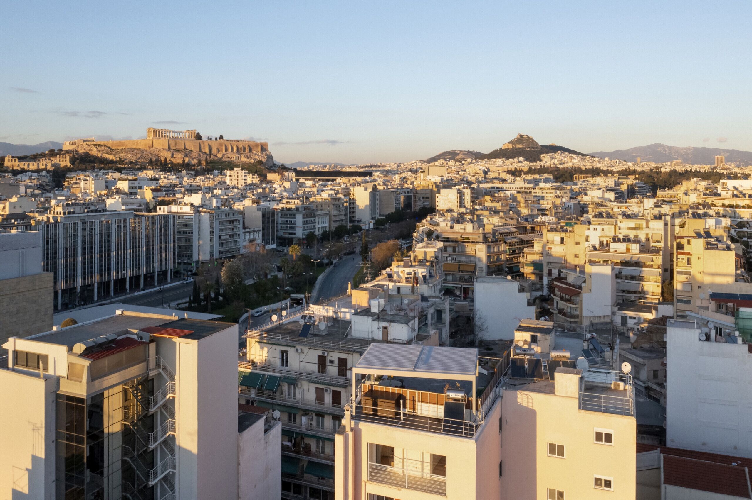 Un paysage urbain avec un bâtiment historique imposant situé sur une colline, des bâtiments modernes et une route sinueuse.