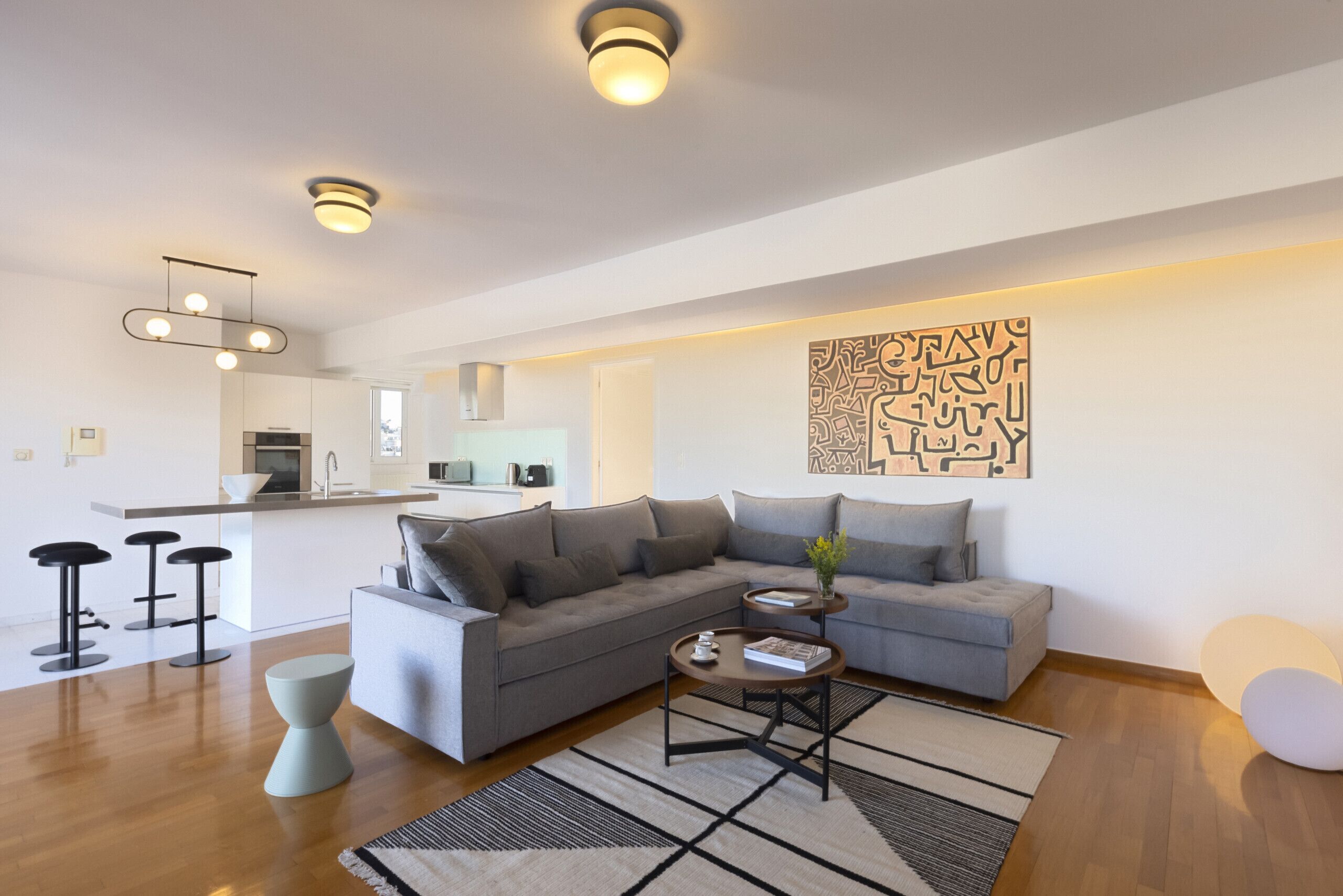 A modern living room with a grey sectional sofa, a coffee table, and a kitchen in the background.