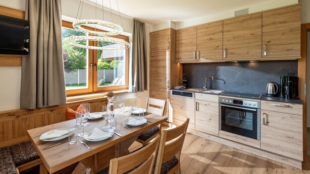 Une cuisine moderne avec des meubles en bois, un four encastré et un coin repas avec une table dressée pour quatre personnes.