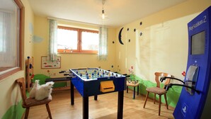 Une pièce avec une table de baby-foot, une console PlayStation 2, une petite chaise et une fenêtre avec des rideaux.