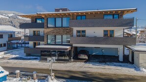 Une maison moderne à plusieurs étages, dotée d’un garage, de grandes fenêtres et offrant une vue sur des montagnes enneigées.