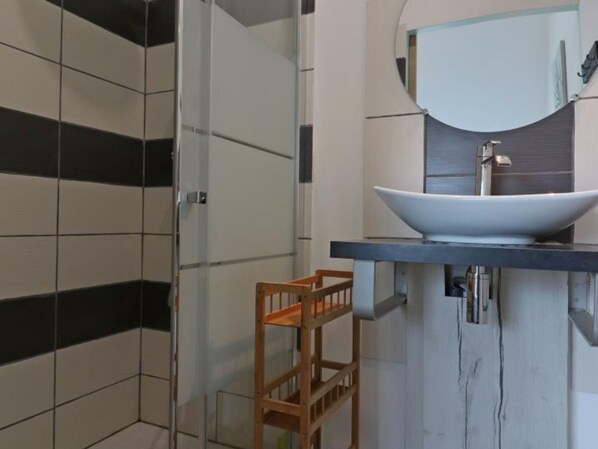 A modern bathroom with a large vessel sink, a glass shower enclosure, and a wooden stool.