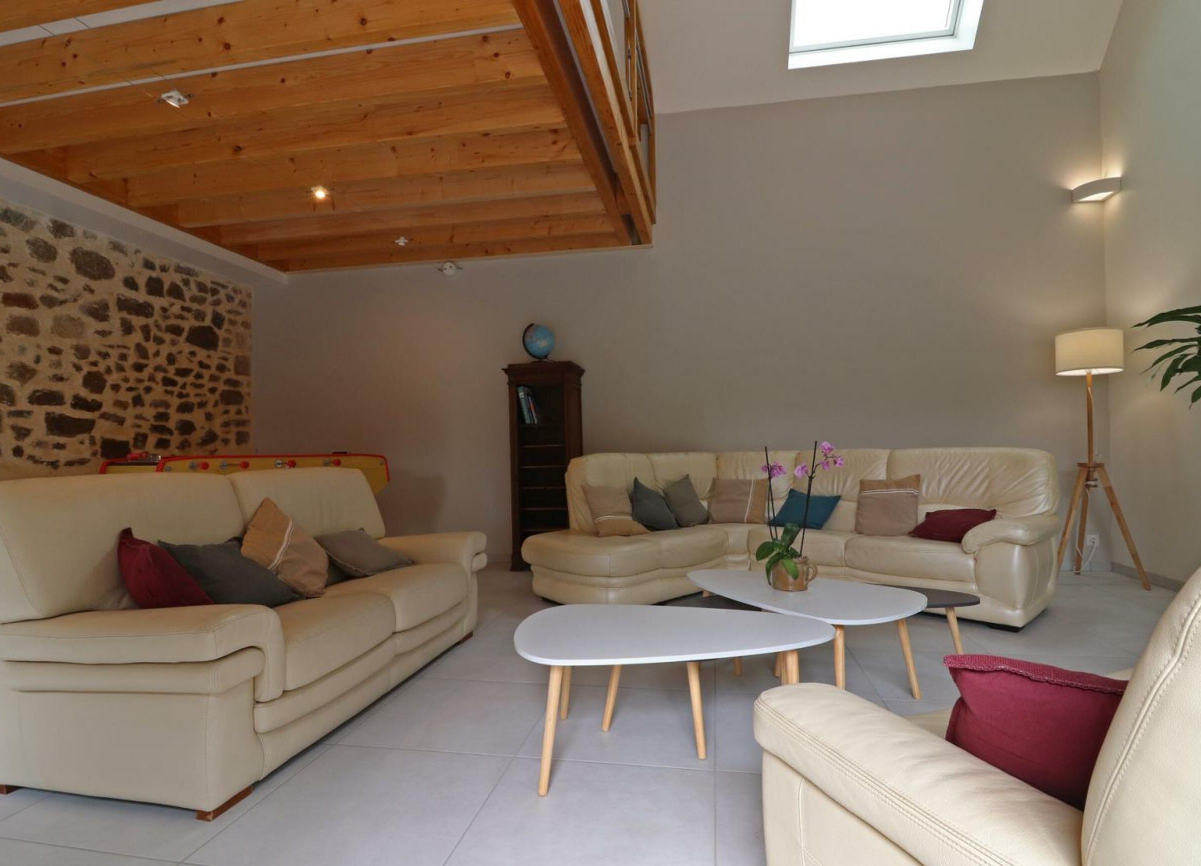 Un salon spacieux avec un mur en pierre, un plafond en bois et une grande fenêtre.