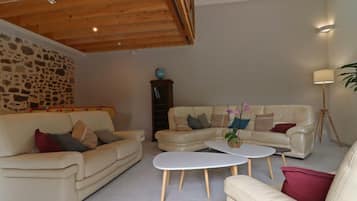 Un salon spacieux avec un mur en pierre, un plafond en bois et une grande fenêtre.