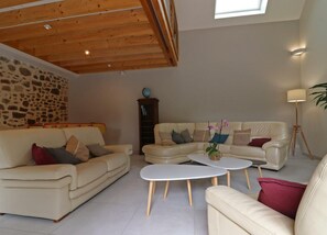 A spacious living room with a stone wall, a wooden ceiling, and a large window. - Spacious family house with sauna and garden (Rives-d'Andaine)