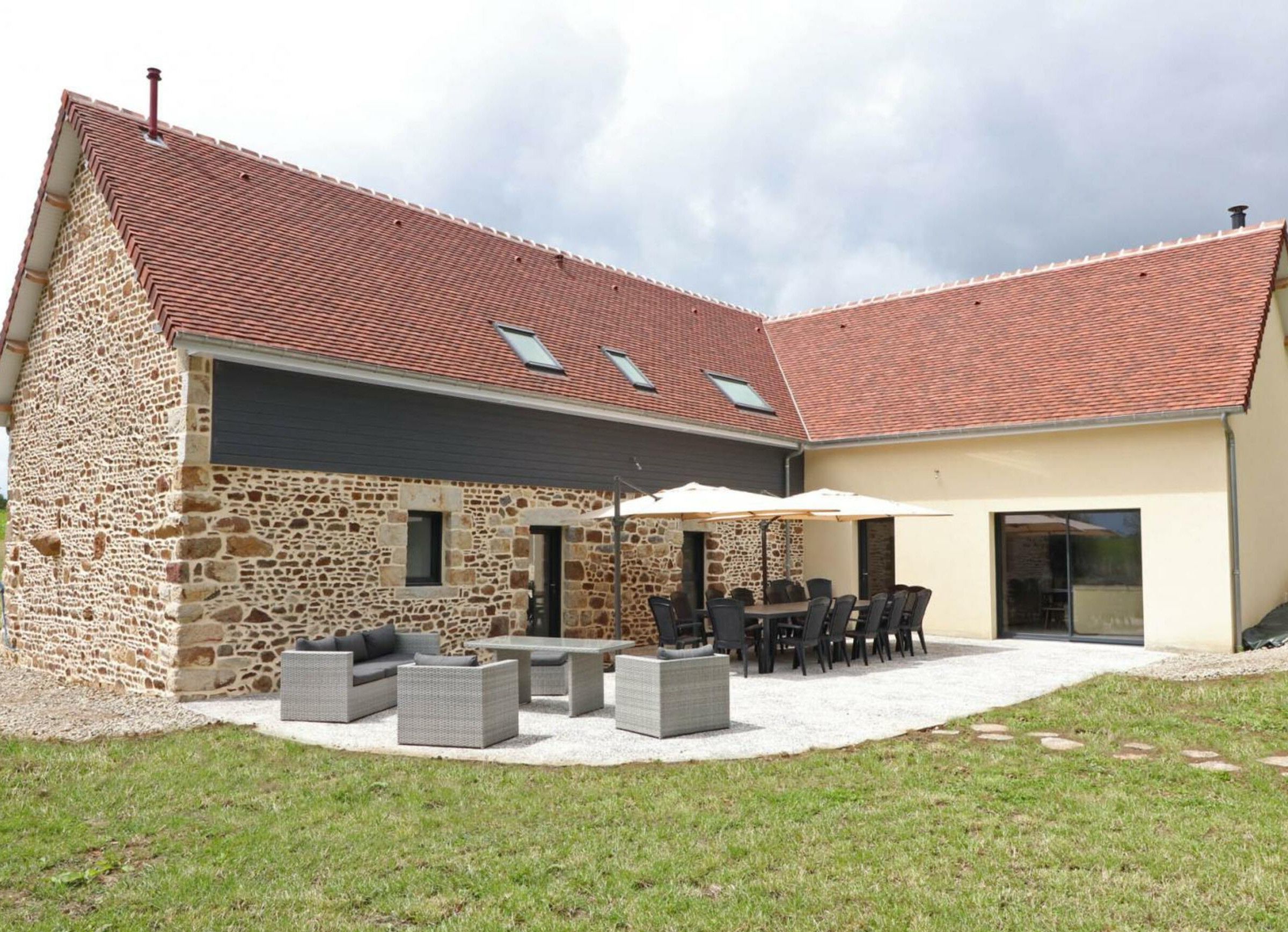 Une maison en pierre avec un toit en tuiles, un espace extérieur aménagé pour s’asseoir et une terrasse couverte.