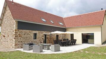 Une maison en pierre avec un toit en tuiles, un espace extérieur aménagé pour s’asseoir et une terrasse couverte.